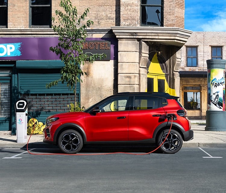 Ein rotes Auto wird an einer Ladesäule am Straßenrand in einer städtischen Umgebung aufgeladen.
