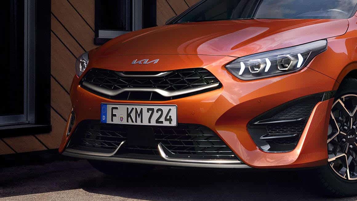 Auf diesem Bild ist die Vorderseite eines orangen Kia-Fahrzeugs mit einem deutschen Kennzeichen zu sehen.