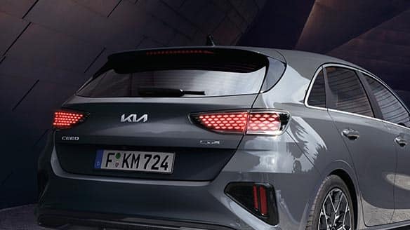 Das Bild zeigt die Rückansicht eines grauen Kia Ceed mit leuchtenden Rückleuchten und einem deutschen Kennzeichen.