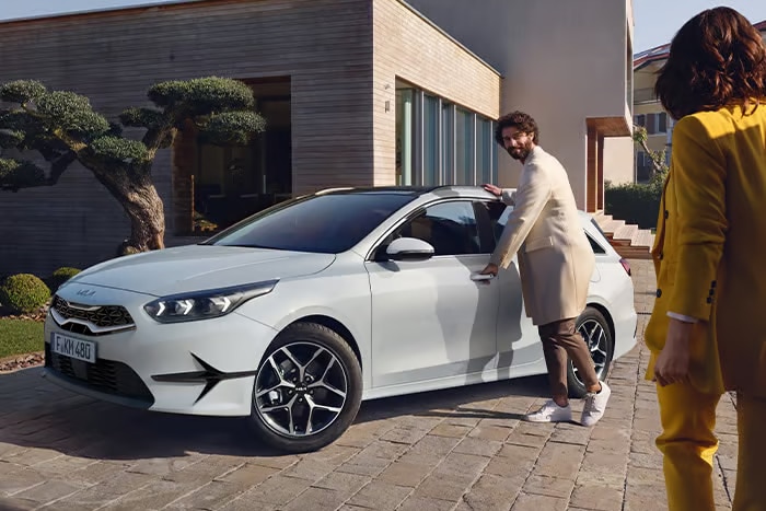 Auf diesem Bild ist ein Mann zu sehen, der einer Frau die Tür eines weißen Autos vor einem modernen Haus öffnet.