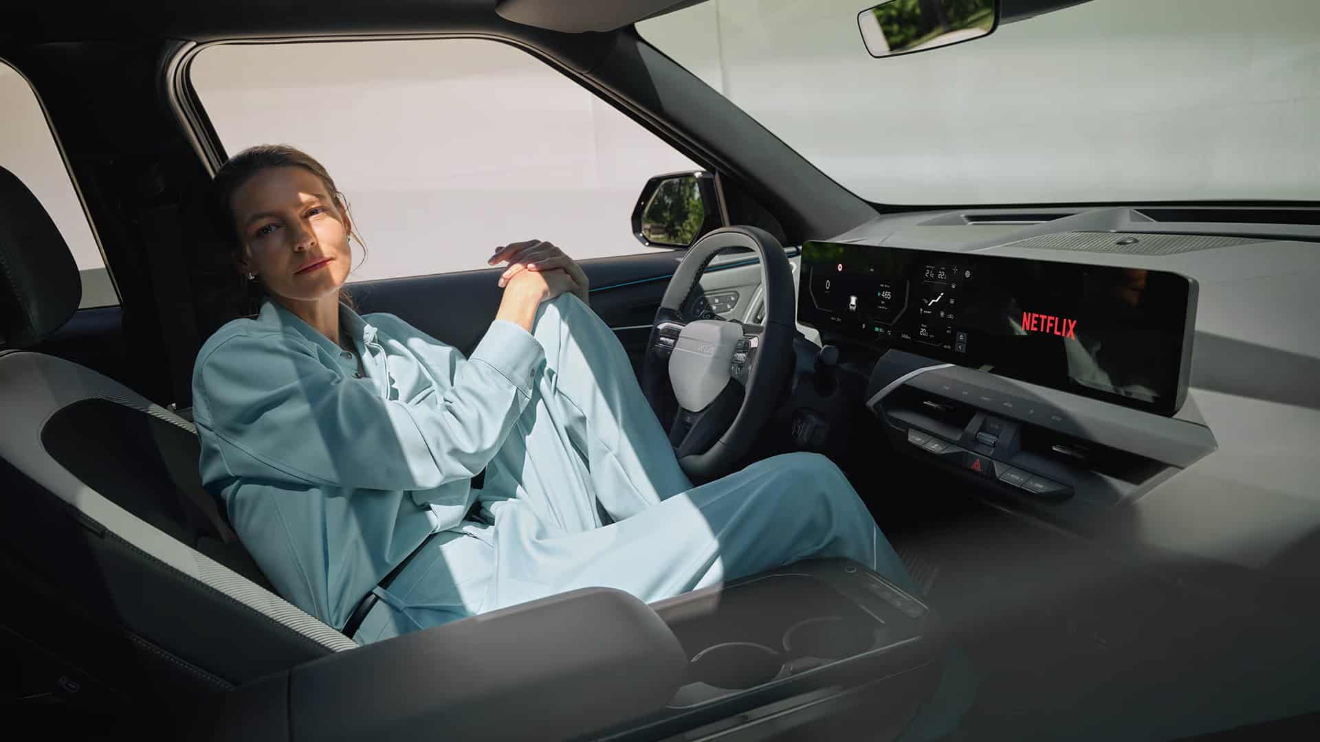 Auf diesem Bild ist eine entspannte Frau in einem modernen Autoinnenraum zu sehen, während auf dem digitalen Bildschirm 'NETFLIX' angezeigt wird.