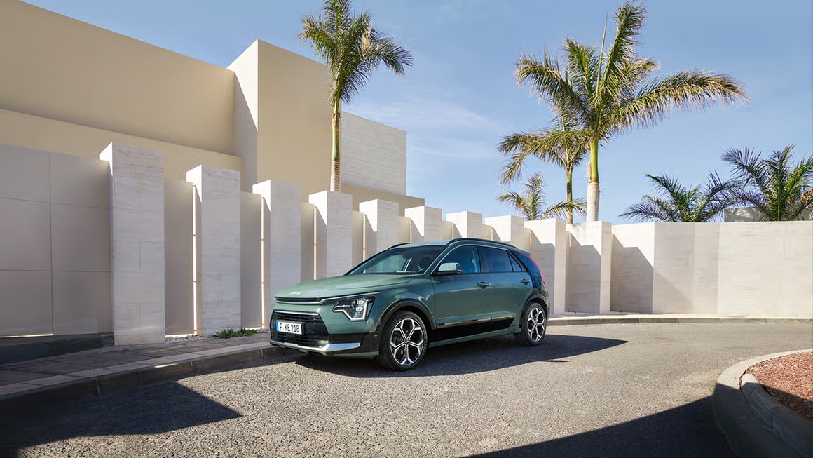 Auf diesem Bild ist ein grünes Auto vor einem modernen Gebäude mit hohen Säulen und Palmen unter blauem Himmel zu sehen.