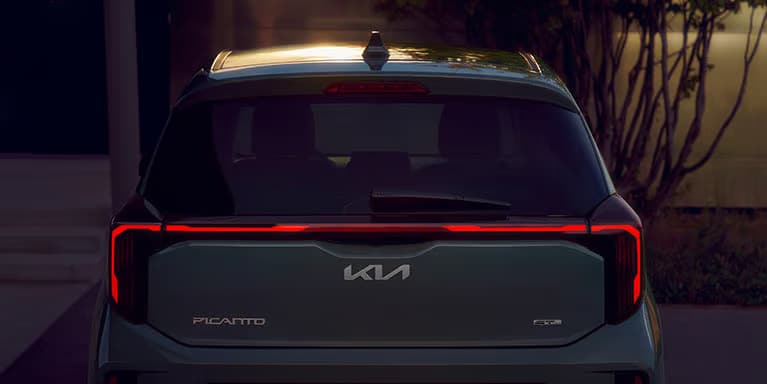 Es ist die Heckansicht eines Kia Picanto GT-Line mit markanten, durchgehenden LED-Rückleuchten im Dämmerlicht zu sehen.