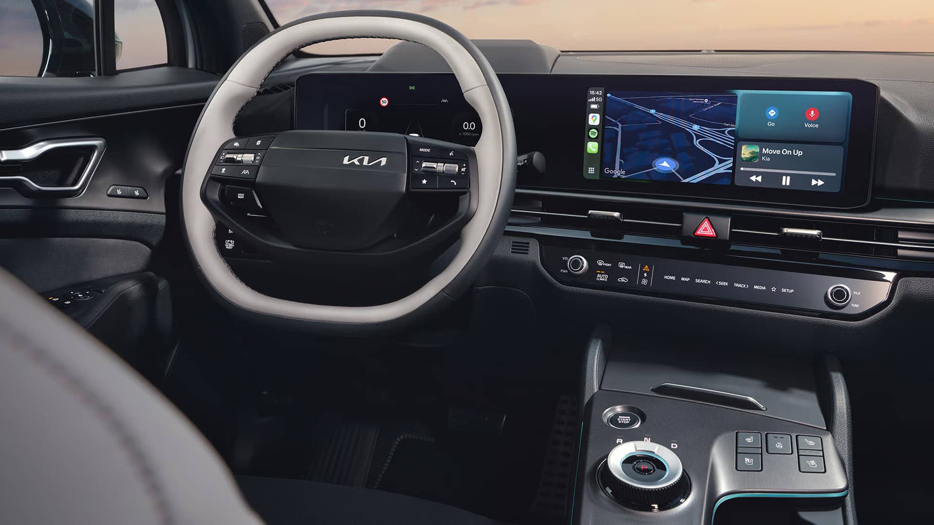 Auf diesem Bild ist das moderne und digitale Interieur eines Autos zu sehen, einschließlich des Lenkrads, der großen Bildschirme für Armaturen und Infotainment sowie der Mittelkonsole mit Drehschalter für die Gangwahl.