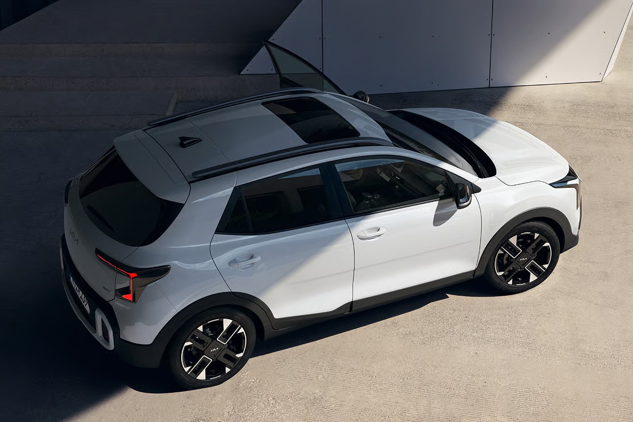 Auf diesem Bild ist ein weißer Kia SUV mit Schiebedach aus der Vogelperspektive auf einer grauen Betonfläche zu sehen.