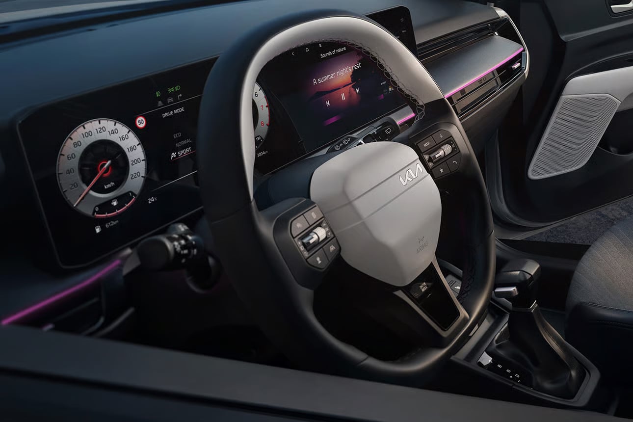 Auf diesem Bild ist der moderne Innenraum eines Fahrzeugs mit Lenkrad, digitalen Armaturen, einem Infotainment-Bildschirm und rosafarbener Ambientebeleuchtung zu sehen.