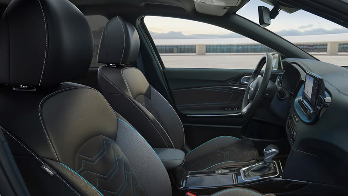 Auf dem Bild ist der sportlich-moderne Innenraum eines Autos mit schwarzen Sitzen, blauen Akzenten und einem Blick nach draußen zu sehen.