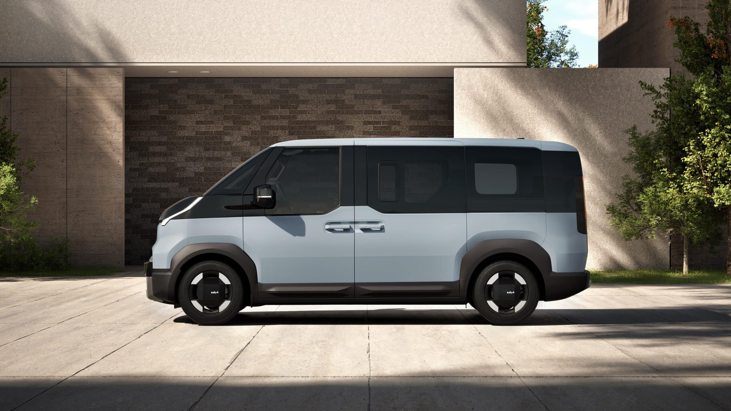Hellblauer Kia PV5 Passenger Elektro-Van in der Seitenansicht, geparkt auf einer gepflasterten Fläche vor einem modernen Gebäude