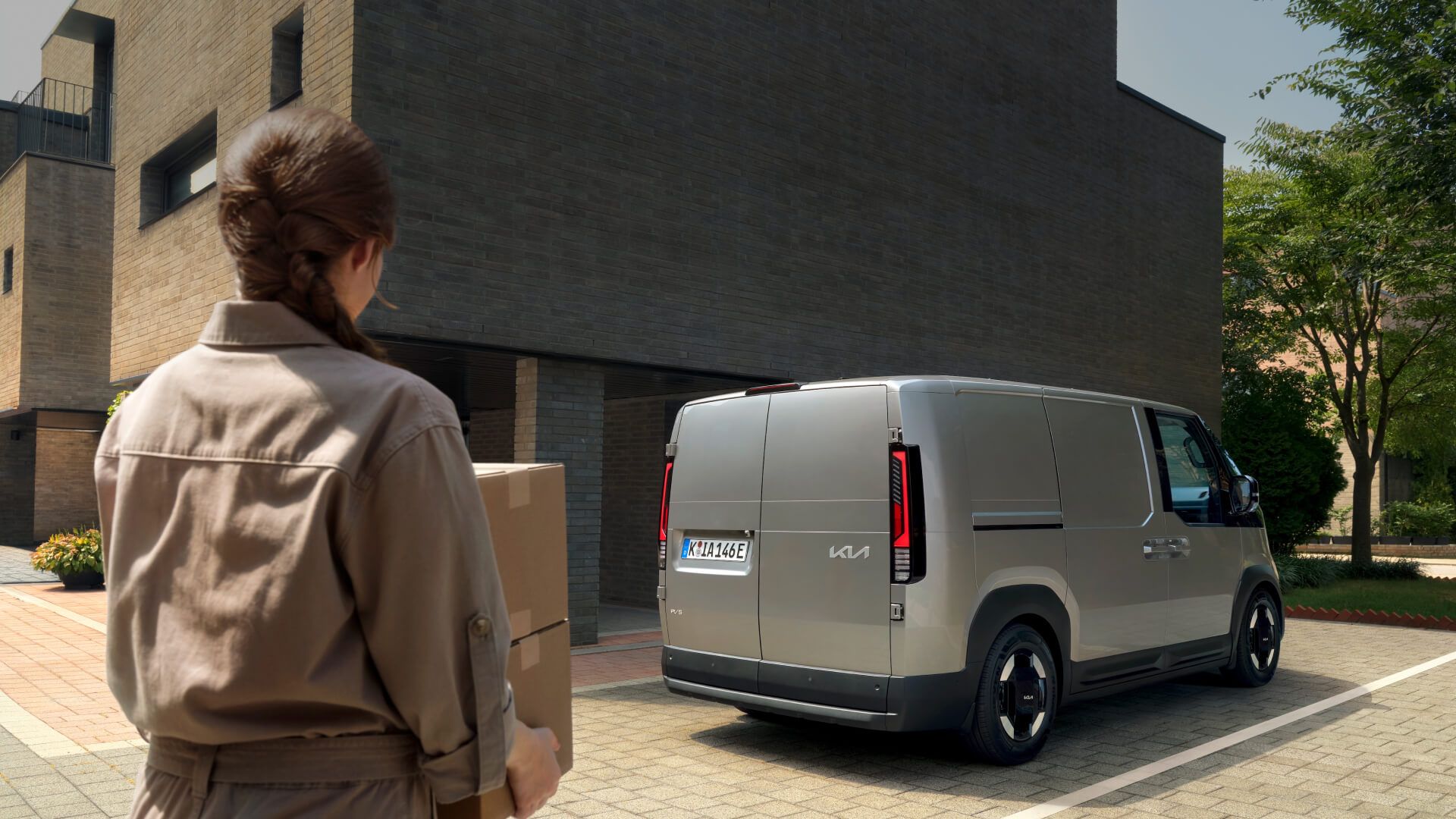 Kia PV5 Cargo Elektro-Van Exterior: Heckansicht des silbernen Fahrzeugs bei einer Warenlieferung vor einem modernen Backsteingebäude.