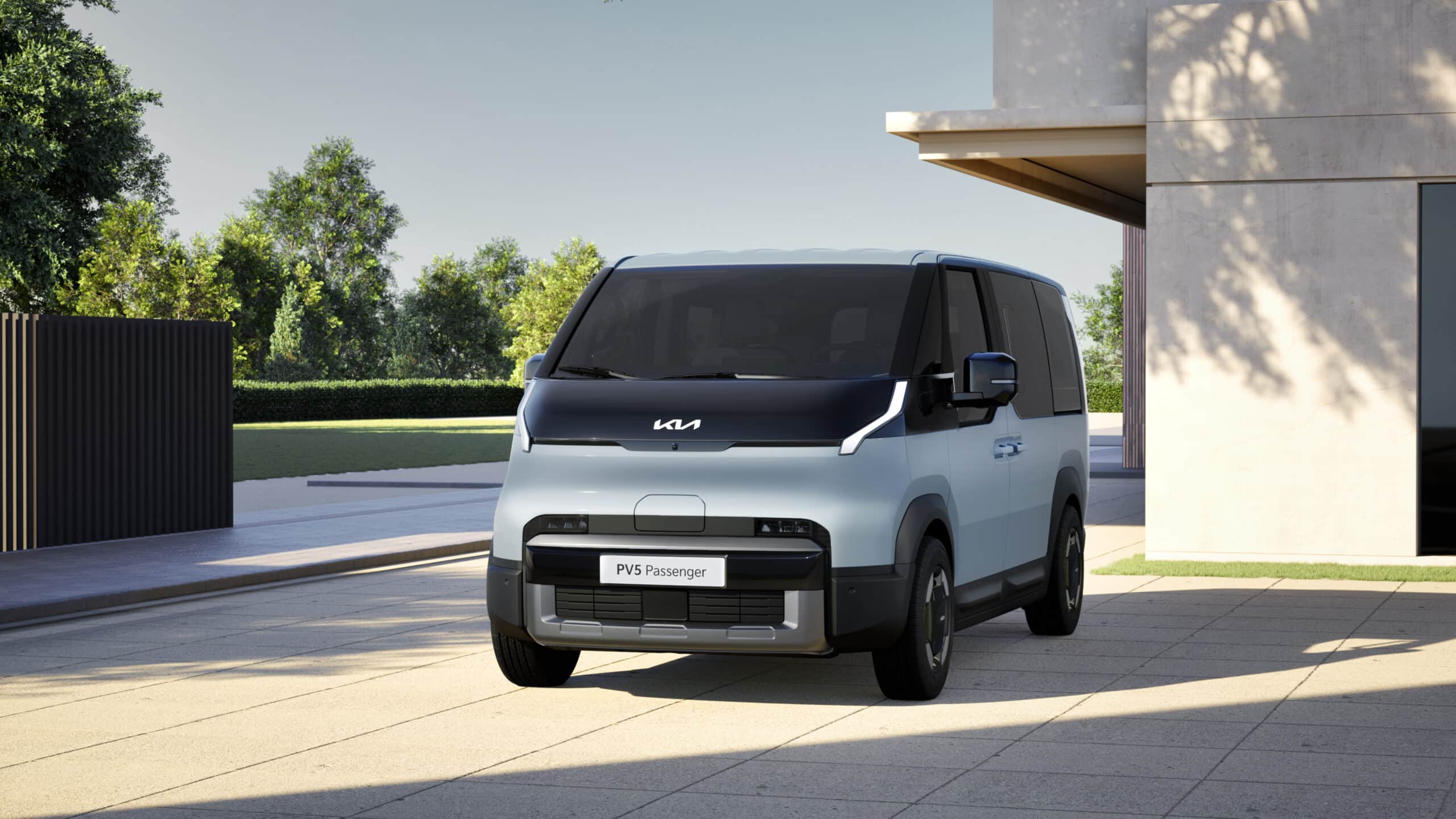 Hellblauer Kia PV5 Passenger Elektro-Van in der Dreiviertel-Frontansicht, geparkt auf einer gepflasterten Fläche vor einem modernen Gebäude