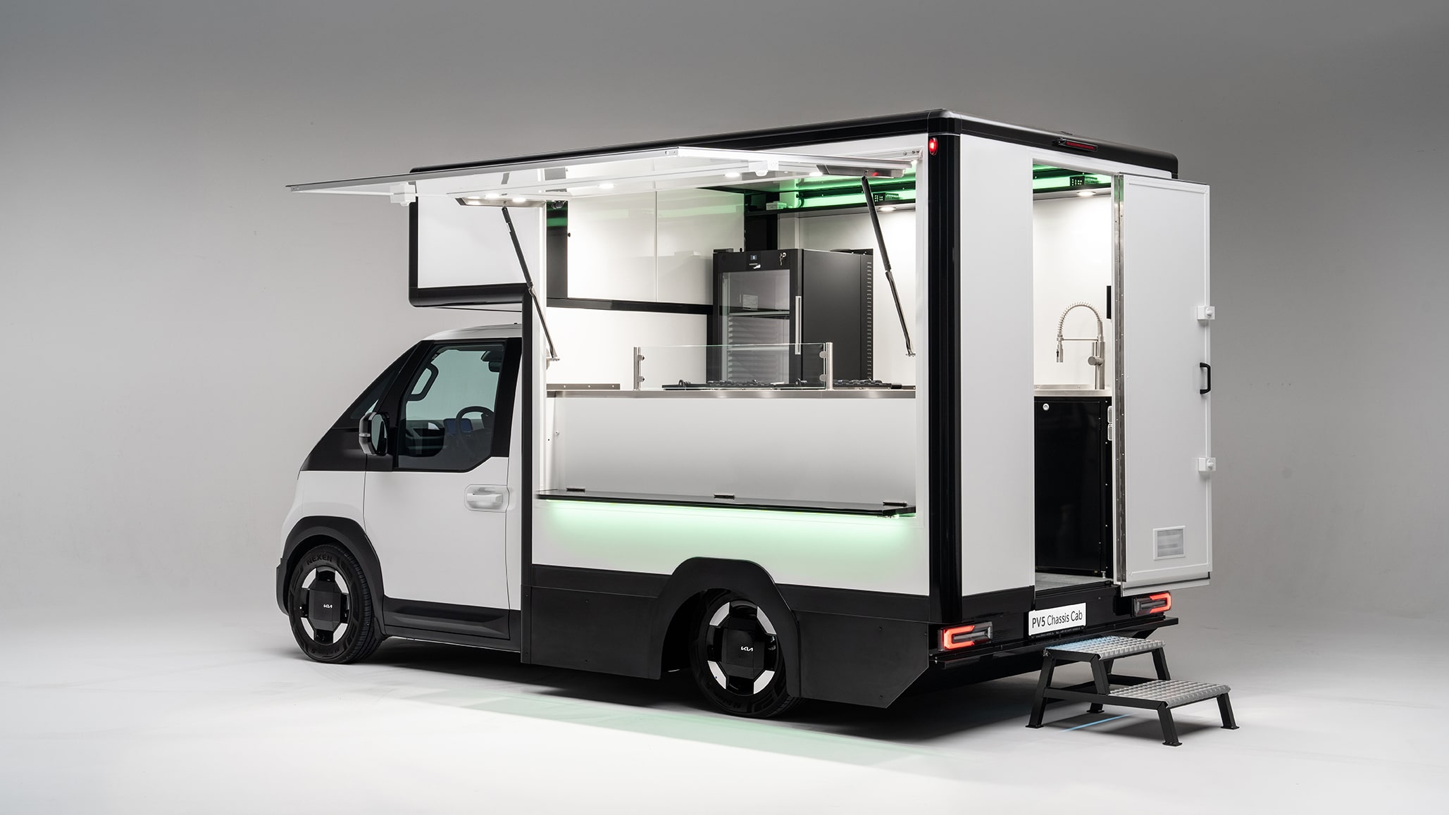 Ein weißer Kia PV5 Chassis Cab Elektro-Transporter, der als Foodtruck oder mobiler Verkaufsstand mit geöffneter Seitenklappe und Innenausstattung (Kühlschrank, Spüle) konfiguriert ist